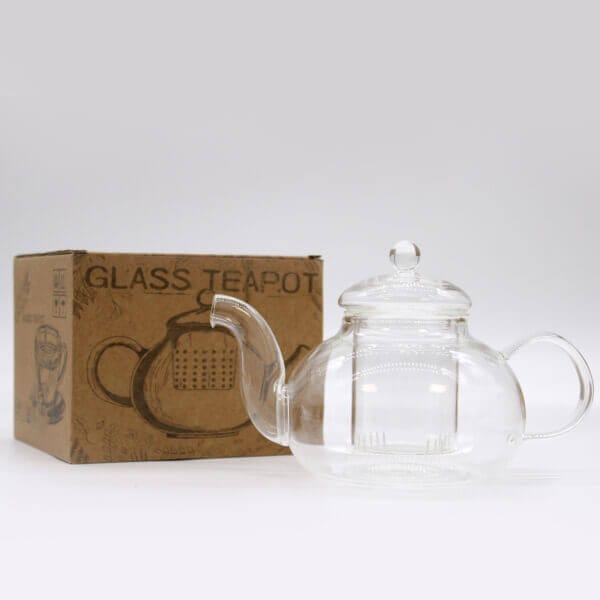 A clear glass teapot with a lid is placed next to a brown cardboard box labeled "GLASS TEAPOT" on a plain white background.