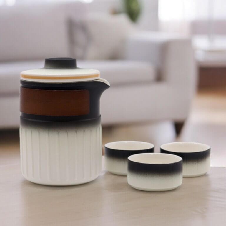 Ceramic teapot with a wooden band and matching gradient cups placed on a light-colored table in a modern living room setting.