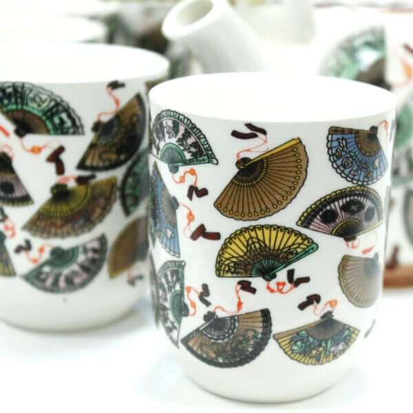White ceramic cups decorated with colorful hand fan patterns and red accents, placed next to each other on a white surface.