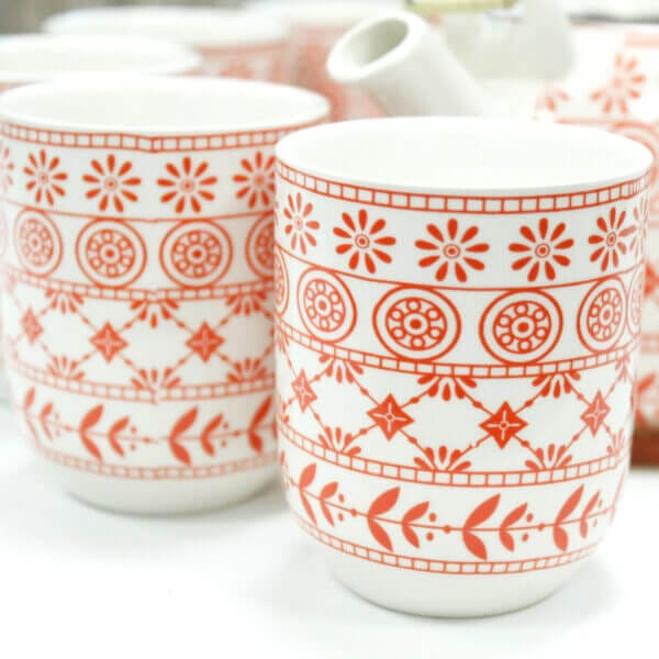 White ceramic cups with red geometric and floral patterns, grouped together on a white surface.