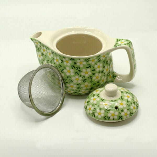 A ceramic teapot with a green and white floral pattern, shown with its lid and a metal tea infuser placed beside it.